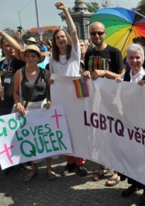 Sister Jeannine Gramick marching alongside individuals at Prague Pride for faith and inclusion, holding a banner that reads “LGBTQ věřící” (“LGBTQ believers”).