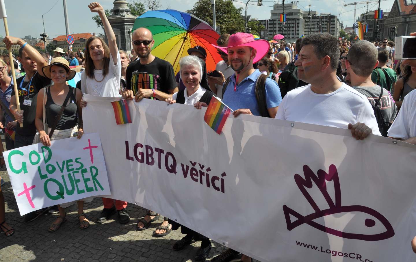 Sister Jeannine Gramick marching alongside individuals at Prague Pride for faith and inclusion, holding a banner that reads “LGBTQ věřící” (“LGBTQ believers”). 